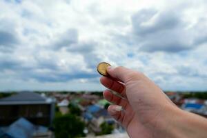 ett hand innehar en mynt. till visa hans använda sig av av pengar de bakgrund är de stad. och de blå himmel omslag foto