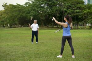 ung kvinna spelar badminton med senior man i de park, dotter spendera utomhus aktiviteter med henne far, koncept människor livsstil, sport och rekreation, familj, familj relation foto