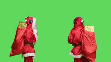 Lycklig man i santa kostym dans, lyssna till musik med väska av gåvor över grönskärm. glad vinter- karaktär har roligt med headsetet klädd i känd röd kostym med vit skägg. foto