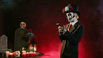 kuslig ung kvinna bläddring internet på smartphone, bär kostym och hatt till fira mexikansk halloween dag. santa muerte modell använder sig av uppkopplad hemsida på mobil telefon, textning meddelanden. foto