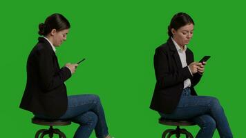stänga upp av affärskvinna bläddring internet på mobil telefon, verkande tillfällig på stol i studio. företag arbetstagare i kostym använder sig av smartphone app till text meddelanden, full kropp grönskärm bakgrund. foto