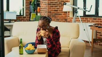 glad person äter hamburgare från snabb mat ta ut, njuter måltid med burger och frites medan hon klockor filma eller komedi visa på tv. kvinna tjänande hämtmat leverans mat på Hem. foto