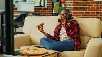 Lycklig kvinna äter pizza från leverans på Hem, njuter film på tv med öl flaskor och snabb mat hämtmat. modern person har roligt binge tittar på visa på tv, ta ut. foto