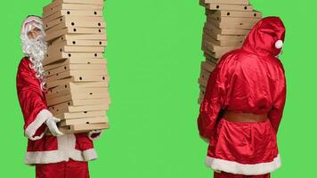 xmas karaktär med stack av pizza lådor, bärande stor lugg av leverans mat, person bär festlig karaktär santa claus kostym med vit skägg. man stående över grönskärm. foto