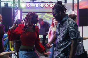 ung afrikansk amerikan par dans och framställning rör sig till leva musik takter i fullt med folk nattklubb. pojkvän och flickvän dansare festa tillsammans på dansgolv i mörk klubb foto