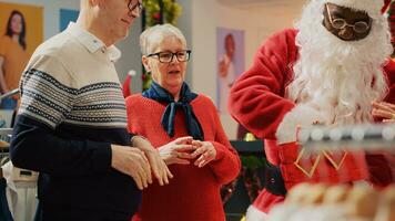 klienter deltar i jul lotta ut håll förbi detaljhandeln assistent klädd som santa claus i festlig utsmyckad Kläder Lagra. tur- äldre par upphetsad efter vinnande PR mode affär tävling foto