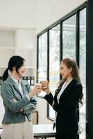 Lycklig två asiatisk företag kvinna innehav kaffe kopp i coworking kontor foto