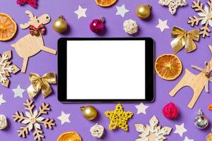 topp se av digital läsplatta omgiven med ny år leksaker och dekorationer på lila bakgrund. jul tid begrepp foto