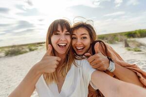 två kvinnor leende och Framställ för de kamera på de strand foto
