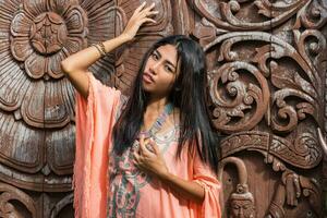 fantastisk asiatisk kvinna i boho etnisk klänning Framställ över trä dekorativ bakgrund. ser på kamera. foto