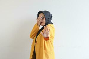 skön ung asiatisk muslim kvinna, bär glasögon och gul blazer beläggning 1 sida av ansikte med hand foto