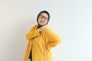 skön ung asiatisk muslim kvinna, bär glasögon och gul blazer har ryggvärk foto