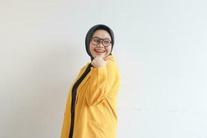 ung skön asiatisk muslim kvinna, bär glasögon och gul blazer med Lycklig leende ansikte uttryck foto
