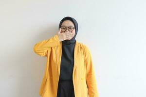 skön ung asiatisk muslim kvinna, bär glasögon och gul blazer med stängd mun gest foto