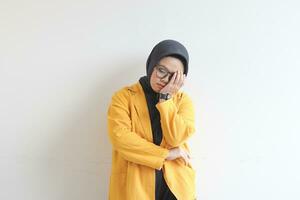 skön ung asiatisk muslim kvinna, bär glasögon och gul blazer beläggning 1 sida av ansikte med hand foto