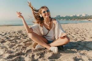 ung attraktiv blond leende kvinna på semester Sammanträde på strand foto