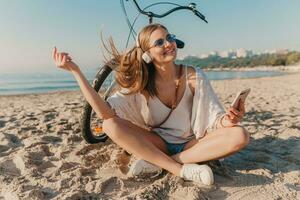 ung attraktiv blond leende kvinna på semester Sammanträde på strand foto