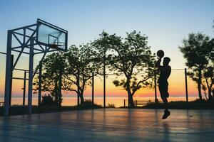svart man håller på med sporter, spelar basketboll på soluppgång, Hoppar silhuett foto