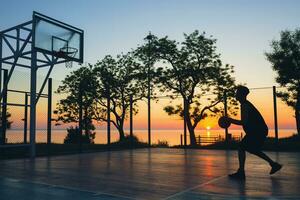 Häftigt svart man håller på med sporter, spelar basketboll på soluppgång, silhuett foto