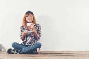 glad kvinna som sitter på trägolv med kaffemugg isolerad på vit bakgrund foto
