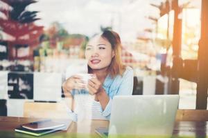 hipster kvinna som håller en kopp kaffe och arbetar i café foto