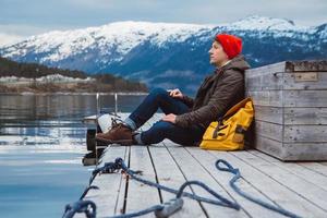 resenär man sitter på träbrygga på bakgrund av berg och sjö foto