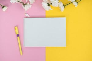 en rena anteckningsbok och penna på en ljus rosa och gul tabell. attrapp med en bukett av blommor foto
