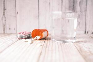 medicinskt piller, blisterförpackning och ett glas vatten på bordet foto