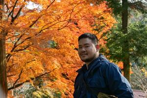 asiatisk man under lönn träd löv under höst med Färg förändra på blad i orange gul och röd, faller naturlig bakgrund foto