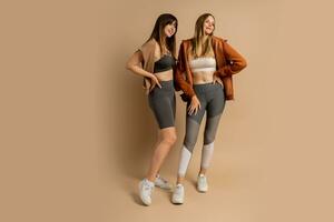 två sportigt kvinnor i eleganta kondition cwear Framställ på beige bakgrund. friska livsstil begrepp. full längd. foto
