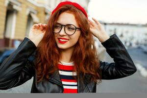eleganta ung ingefära kvinna i röd basker och glasögon Framställ på de gata. foto