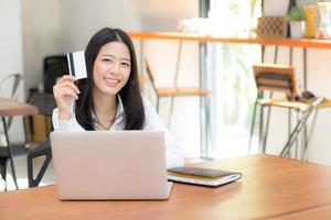ung asiatisk kvinna som håller ett kreditkort och handlar online på bärbar dator.