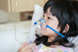 sjuk liten asiatisk flicka inandning med nebulisator för respiratorisk behandling foto