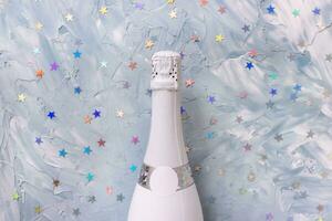 vit champagne fest flaska och colorul metallisk stjärnor konfetti på blå bakgrund. platt lägga, kopia Plats. ny år och jul firande begrepp foto