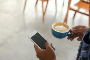 stänga upp av asiatisk man innehav en kopp av kaffe och mobil telefon. teknologi och morgon- rutin- begrepp foto