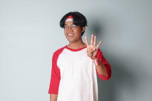 porträtt av attraktiv asiatisk man i t-shirt med röd och vit band på huvud, räkning fyra med fingrar. isolerat bild på grå bakgrund foto