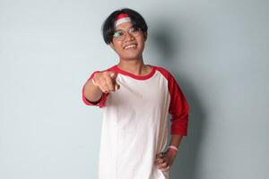 porträtt av attraktiv asiatisk man i t-shirt med röd och vit band på huvud, pekande framåt- på de kamera. isolerat bild på grå bakgrund foto