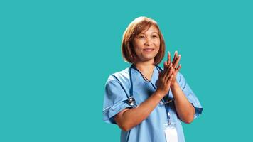 godkännande leende sjuksköterska lyckligt applåder händer, nöjd med prestationer. klinik anställd glädjande, håller på med applåderar gest medan på arbete, isolerat över studio bakgrund, stänga upp foto