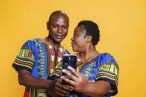 afrikansk amerikan fru och Make par innehav mobil telefon och tar selfie. leende man och kvinna par framställning Foto på mobil telefon främre kamera tillsammans på studio bakgrund