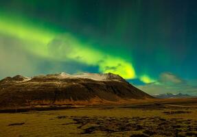 aurora borealis och massiv bergen i island. lysande nordlig lampor skapande Fantastisk nordic landskap under stjärnor på himmel. färgrik magisk fenomen med kullar, natt fotografi. foto