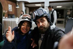 ung gäster fångande vinter- äventyr med selfies på smartphone. blandning av teknologi och semester i vintertid för par i snö Kläder åka skidor glasögon och hjälm på exklusiv berg tillflykt. foto