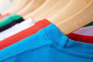 mode t-shirt på Kläder kuggstång - närbild av ljus färgrik garderob på trä- galgar i Lagra garderob. foto