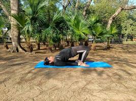 ung indisk kvinna praktiserande yoga utomhus- i en parkera. skön flicka öva grundläggande yoga utgör. stillhet och koppla av, kvinna lycka. grundläggande yoga poser utomhus- foto