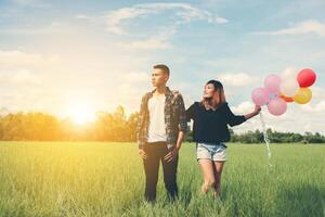 ungt par springer och håller ballongen i det gröna gräset nedanför foto