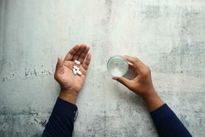 topp se av ung män tar medicinsk piller och innehav en glas av vatten foto