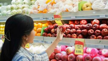 porträtt av en skön asiatisk eller indonesiska kvinna uppköp frukt anordnad på frukt kuggstång i en mataffär foto