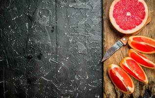 bitar av grapefrukt på en skärande styrelse med en kniv. foto