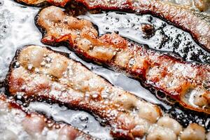 bitar av bacon är friterad i kokande olja med luft bubblor. foto