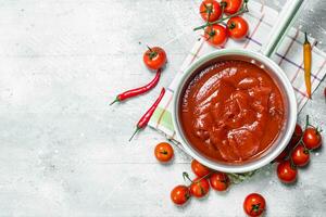 tomat sås i en pott på en servett med en chili peppar och körsbär tomater. foto
