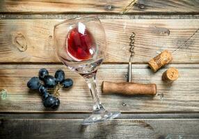 röd vin i en glas med vindruvor och en korkskruv. foto